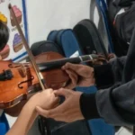 Un niño estudiante de la U.E. Johnny Escobar sosteniendo un violín durante una clase de iniciación musical, mientras un instructor guía la posición de sus manos.