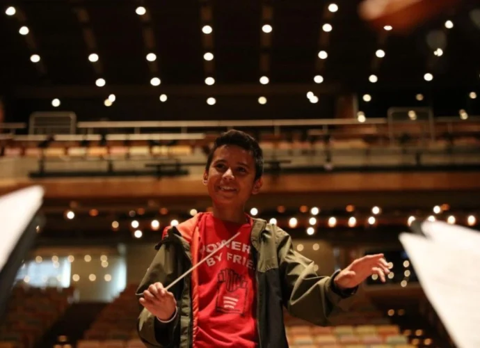 Primer plano de Samuel Abraham González Quintero sonriendo y dirigiendo con batuta en la Sala Simón Bolívar de Caracas, ilustrando el éxito del plan de carrera de Otilca.