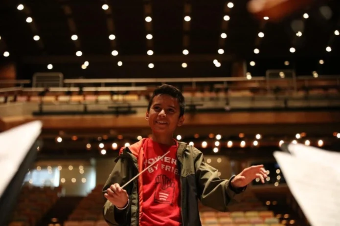 Primer plano de Samuel Abraham González Quintero sonriendo y dirigiendo con batuta en la Sala Simón Bolívar de Caracas, ilustrando el éxito del plan de carrera de Otilca.