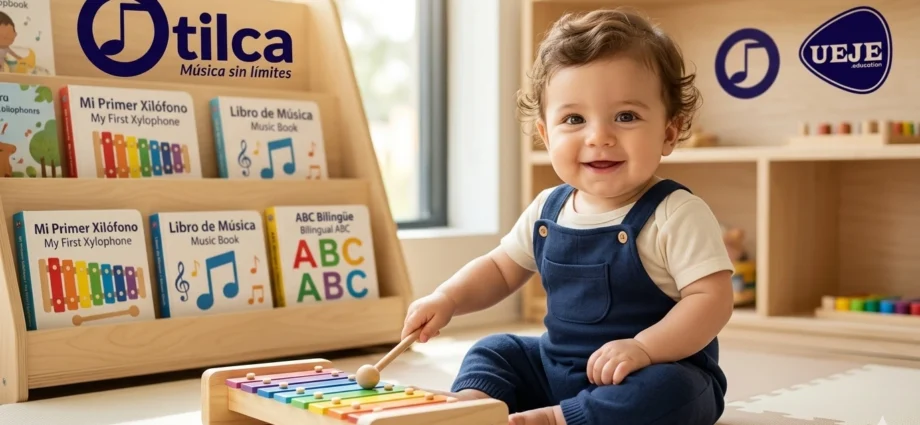 Un bebé sentado en una sala de juegos luminosa, vestido con un peto azul marino, sonríe y toca un xilófono de colores con una baqueta de madera. Detrás de él hay estanterías de madera llenas de libros bilingües con títulos en español e inglés, como "Mi Primer Xilófono" y "Mi Libro de Música". Los logotipos de "Otilca - Música sin límites" y "UEJE" son visibles en los estantes.